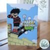 Personalised Dennis menace cannon birthday card template with 'Happy Birthday' text and space for a name, ideal for custom celebrations.